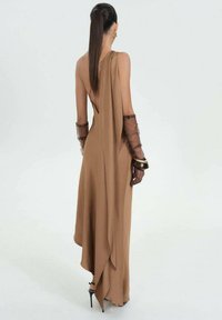 Brun udenærmofor gown med en asymmetrisk drapering, åben ryg og gennemsigtige sorte handsker. Har en glat tekstur og en gulvlængde design.