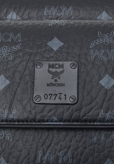 Zwarte leren tas met textuur, voorzien van een geperst MCM-logo patroon en een metalen plaatje met de tekst "MCM MÜNCHEN 07741."
