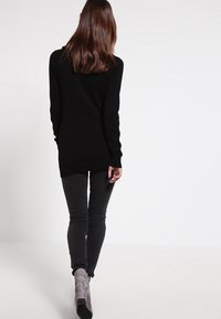 Černý svetr s dlouhým rukávem a volným střihem, kombinovaný s tmavě šedými skinny džíny a světle šedými kotníkovými botami. Minimalistický design.