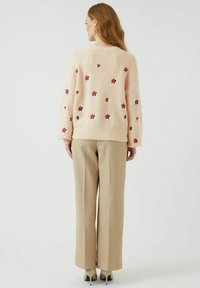 Svijetloružičasti pleteni pulover s izvezenim cvjetovima na leđima, uparen s bež hlačama širokih nogavica i cipelama s visokom petom.