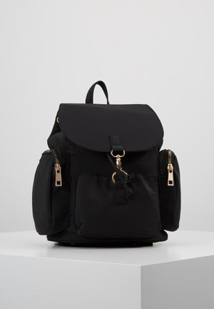 Schwarzer Rucksack mit oberer Klappe, Fronttasche, zwei seitlichen Reißverschlusstaschen und einer Schlaufe als Griff auf einer weißen Präsentationsfläche.