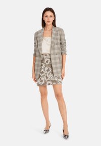 Grau karierter Blazer, cremefarbenes Oberteil, bestickter Rock mit floralen Mustern in Taupe und Weiß, kombiniert mit silbernen spitz zulaufenden High Heels.