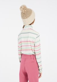 Haut à manches longues et col montant avec des motifs d'arbres multicolores et géométriques, associé à un pantalon rose avec un logo au dos. Bonnet en tricot beige.