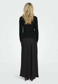 Čierny outfit pozostávajúci z priliehavého topu s textúrovanými pruhmi zebry a splývavou dlhou sukňou. Tkanina je hladká a hodvábna, doplnená o vysoké podpätky.