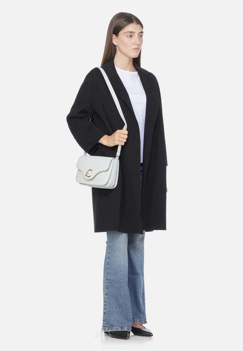 Cappotto nero oversize, t-shirt bianca, jeans blu a zampa d'elefante e scarpe nere appuntite. Porta una borsa grigia chiara con una chiusura dorata.