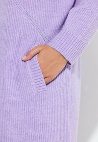 Lawendowy sweter z dzianiny z prążkowanymi mankietami i krawędzią, posiadający boczną kieszeń, podkreślający teksturowaną tkaninę i swobodny design.