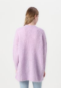 Lilac krāsas pūkains džemperis ar brīvu piegriezumu, garām piedurknēm un struktūrētu adījumu. Iezīmē apaļu kakla izgriezumu un ribu maliņas.