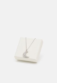 Collier en argent avec un pendentif en forme de croissant de lune orné de pierres scintillantes, présenté sur une boîte à bijoux blanche.