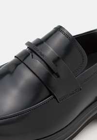 Mocassins en cuir noir avec un design épuré, une bande distinctive et des détails de couture subtils sur le dessus. Marque Calvin Klein visible.