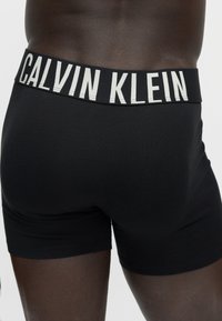 Κοντινό πλάνο ενός ατόμου που φοράει μαύρα μποξεράκια Calvin Klein με το όνομα της επωνυμίας να φαίνεται στη μέση.
