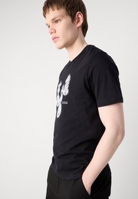 Černé bavlněné tričko s bílým abstraktním grafickým designem na přední straně, krátké rukávy a kulatý výstřih.