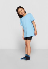 Hele sinine puuvillane T-särk lühikeste varrukatega, koos mustade lühikeste pükste ja tumesiniste sokkidega, millel on sinised aktsendid. Seisavas poosis, neutraalse taustaga.