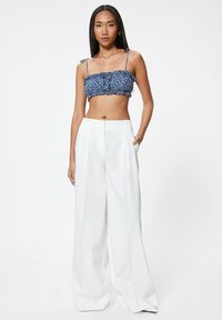 Top corto azul con estampado floral y bordes con volantes, combinado con pantalones blancos de pierna ancha y cintura alta. Tela suave y corte entallado.