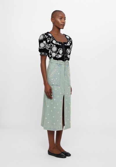 Μαύρο τοπ με φούσκες μανίκια και κέντημα λουλο�υδιών, συνδυασμένο με φως μπλε τζιν φούστα που διαθέτει διακοσμητικά λευκά σχέδια και μπροστινή σχισμή.