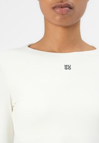 Balta ilgomis rankovėmis palaidinė su apvalia iškirpte ir juodu HUGO logotipu ant krūtinės. Pagaminta iš lygaus, tamprios medžiagos.