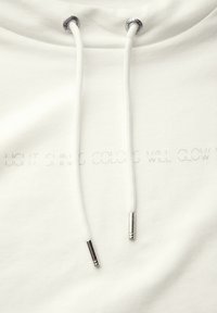 Witte hoodie met een zachte textuur, voorzien van trekkoorden met zilveren metalen punten en subtiele reliëftekst: "LICHT SCHIJNT KLEUREN ZULLEN STRALEN."