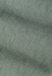 Tissu tissé vert clair et doux avec une texture visible et des plis subtils créant de douces ombres sur la surface.