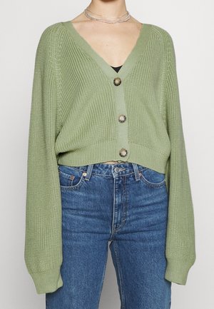 Grøn ribbet strikket cardigan med V-hals, tre knapper og lange ærmer. Kortet pasform parret med højtaljede blå jeans.