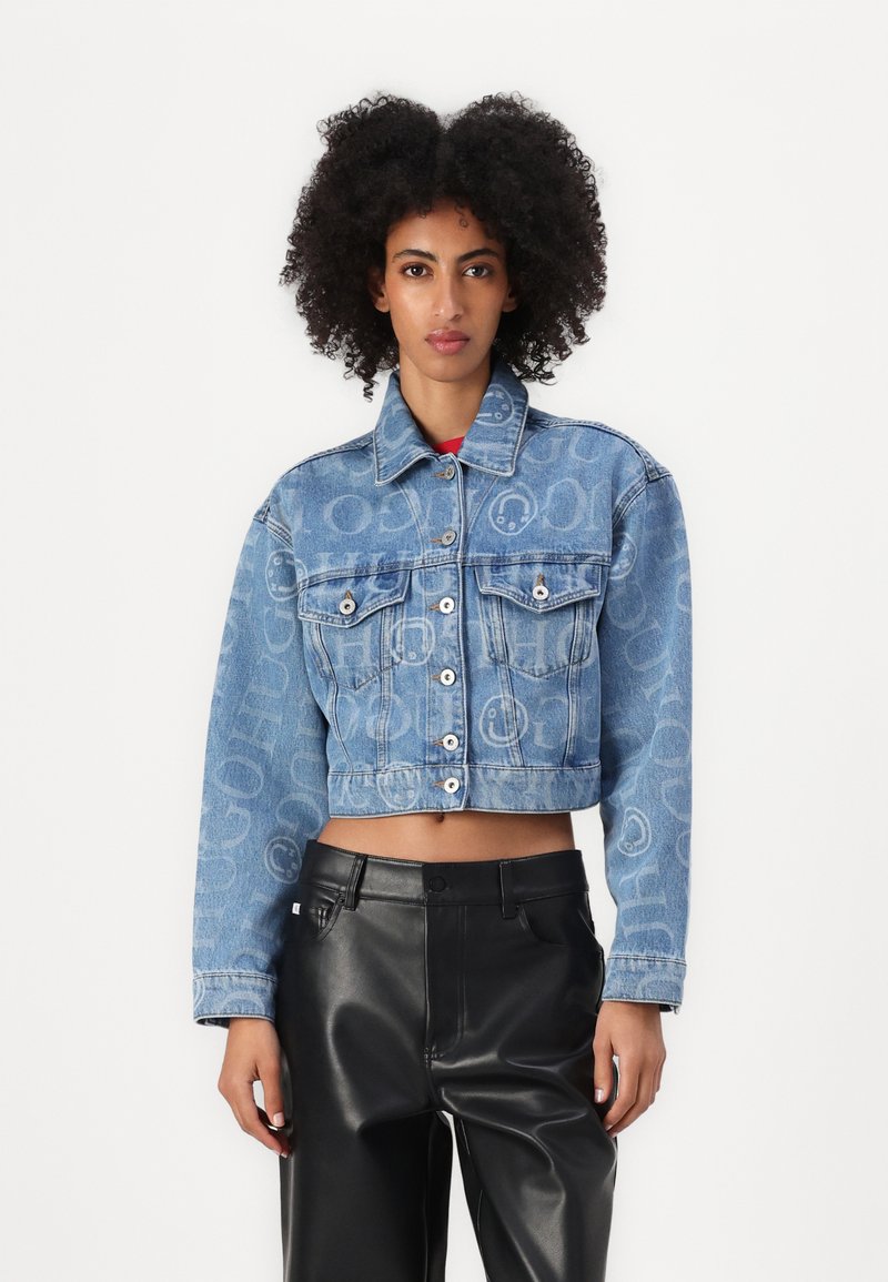 Veste en jean coupée de couleur bleu clair, avec deux poches poitrine, quincaillerie en argent et motifs en relief. Associée à un pantalon en cuir noir.
