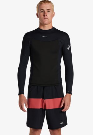 Rash guard de manga larga negro con un diseño ajustado, combinado con bañadores negros que presentan una amplia franja horizontal roja y detalles de logo.