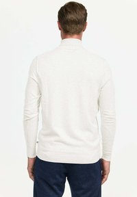 Pull en beige à manches longues avec une texture unie et un col ribbé. Affiche un design ajusté et un ourlet contrastant, porté avec un pantalon sombre.