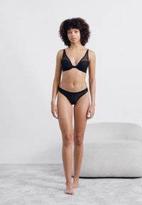 Ensemble de lingerie noire comprenant un soutien-gorge en maille transparente avec des bretelles réglables et un slip bikini assorti. Texture lisse, design simple.