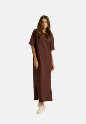 Czerwony długi t-shirt w stylu sukienki z krótkimi rękawami, bocznymi rozcięciami i luźnym krojem, zestawiony z białymi trampkami na neutralnym tle.