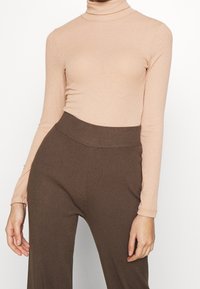 Långärmad polotröja i ljusbeige ribbad tyg som matchas med högmidjade bruna ribbade byxor, med en mjuk textur och en åtsittande design.