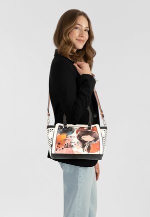 Bolso de mano con un exterior en blanco y negro, que presenta una ilustración colorida y texto en la parte frontal. Dos asas y una correa de hombro desmontable.