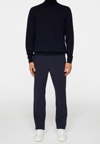 Schwarzer Rollkragenpullover mit langen Ärmeln, kombiniert mit dunkelgrauen, maßgeschneiderten Hosen. Weiße Sneaker vervollständigen das Outfit. Glatte Textur überall.