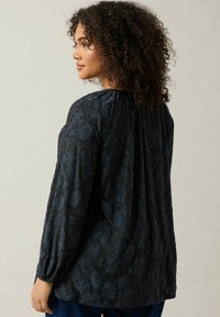 Schwarze Bluse mit Blumenmuster, langen, gerafften Ärmeln und lockerer Passform. Weicher Stoff mit subtiler glänzender Oberfläche. Rückansicht gezeigt.