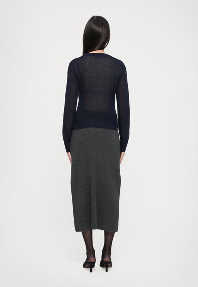 Sweater de manga longa azul-marinho, transparente, com um acabamento texturizado, combinado com uma saia midi cinza. O conjunto apresenta um design simples e elegante.