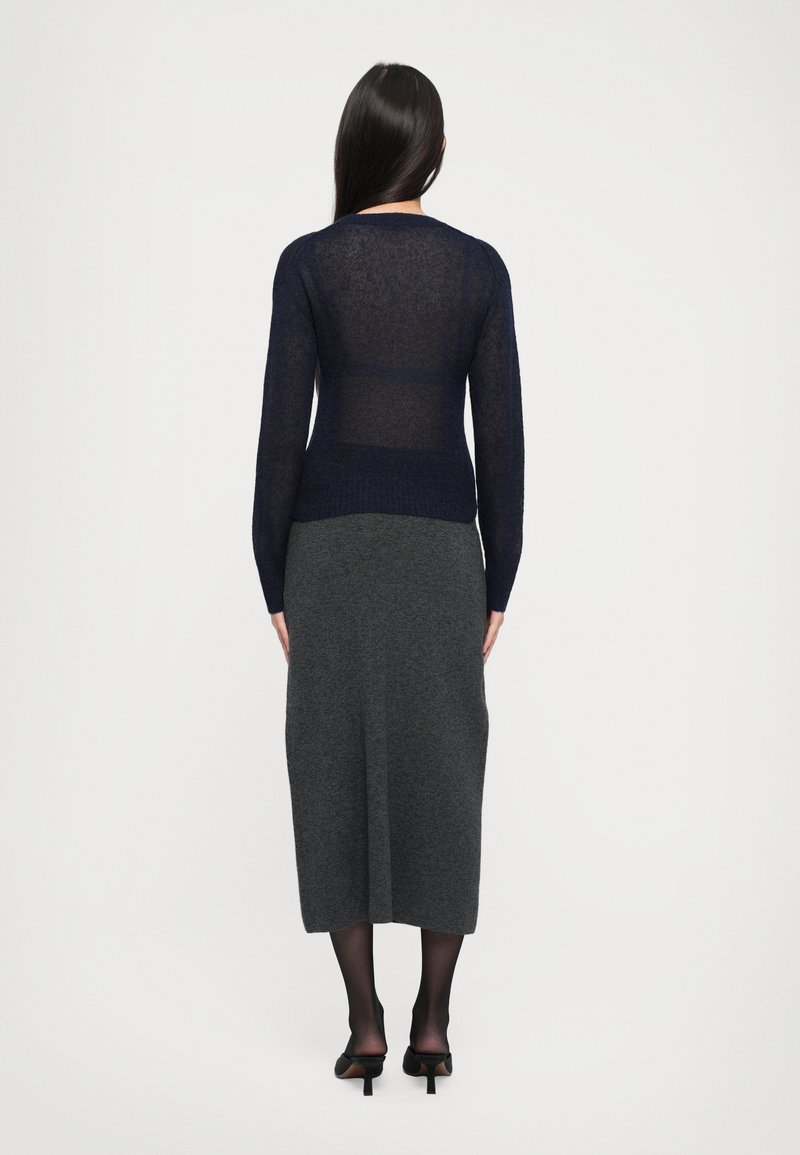 Maglione lungo a maniche lunghe in tessuto traslucido di colore blu navy, abbinato a una gonna midi grigia. L'outfit presenta un design semplice e lineare.
