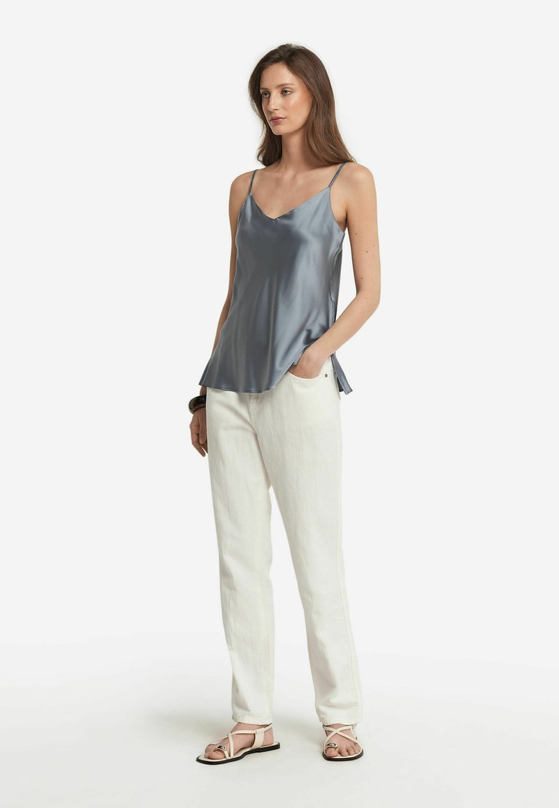 Grå satin-top med tunna axelremmar, rund halsringning och utsvängd nederkant, kombinerad med vita linbyxor och sandaler med remmar.