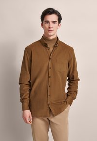 Braunes, knöpfbares Hemd mit weicher Textur und einer Brusttasche, kombiniert mit einem passenden Rollkragenpullover. Das Hemd hat schwarze Knöpfe.