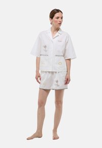 Ensemble comprenant une chemise en lin blanc à manches courtes et un short avec des motifs brodés de soleil et de palmiers. Présente un bord contrastant le long des bords et des poches.