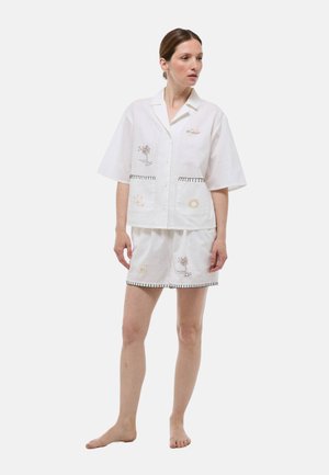 Ensemble comprenant une chemise en lin blanc à manches courtes et un short avec des motifs brodés de soleil et de palmiers. Présente un bord contrastant le long des bords et des poches.