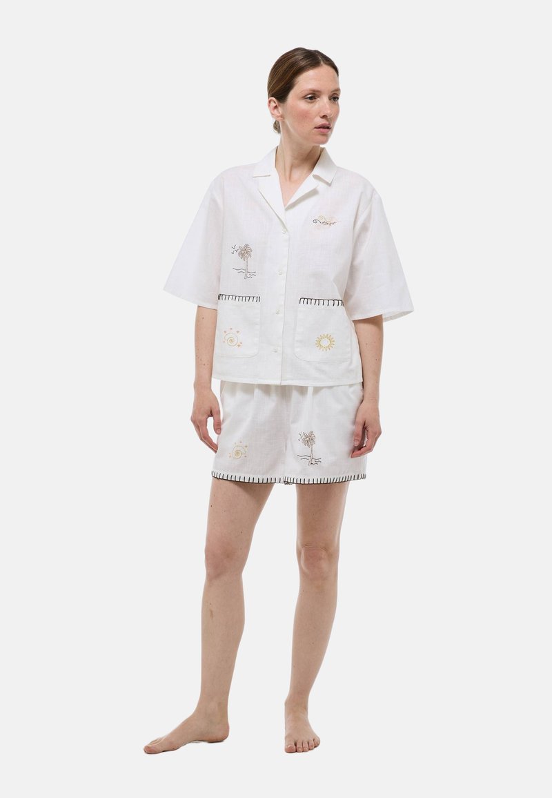 Ensemble comprenant une chemise en lin blanc à manches courtes et un short avec des motifs brodés de soleil et de palmiers. Présente un bord contrastant le long des bords et des poches.
