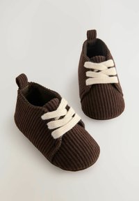 Brune fløjl baby sko med hvide snørebånd, rund tå, ribbet tekstur og en lille løkke bagpå for nem påklædning.