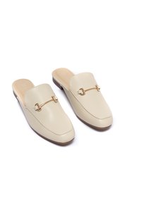 Béžové kožené slip-on mokasíny s špičatou špičkou, doplněné zlatými akcenty a hladkou texturou. Plochá podrážka s minimálním vzorkem.