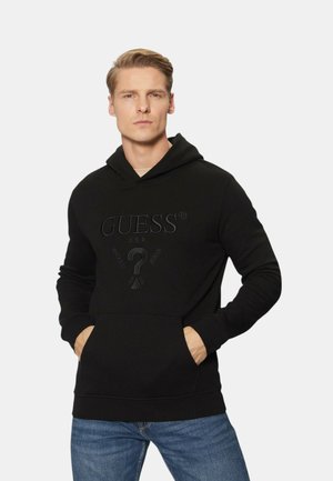 Felpa nera con tasca a marsupio e logo "GUESS" in rilievo. Realizzata in materiale morbido, presenta polsini a coste e cappuccio con lacci.