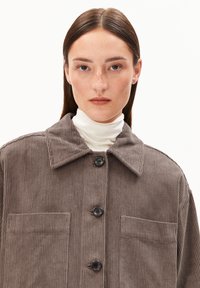 Braune Cordjacke mit Kragen, zwei aufgesetzten Brusttaschen und schwarzen Knöpfen auf der Vorderseite. Weicher Stoff mit vertikalen Streifen.