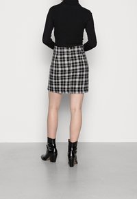 Svart ribbad polotröja, åtsittande ovanför en mönstrad minikjol i svart och vitt rutig. Svart ankellång stövel med spännen och en kraftig klack.