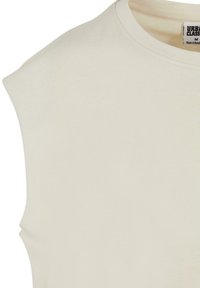 Lys beige ærmeløs t-shirt lavet af blødt bomuld, med en rund halsudskæring og subtile syninger. Ingen mønstre eller dekorative elementer.