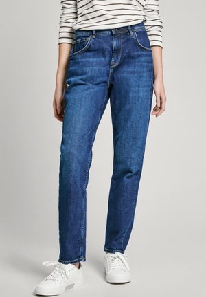 Blaue Jeans aus Denim mit geradem Bein, ausgestattet mit fünf Taschen, Gürtelschlaufen und leichten Nähdetails. Kombiniert mit weißen Sneakers.