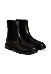 Ein Paar schwarze Lederstiefeletten mit elastischen Seiteneinsätzen und dicken Gummisohlen, vor weißem Hintergrund dargestellt.