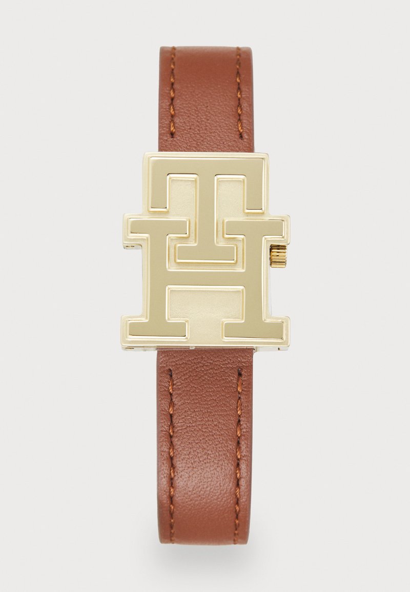 Brown leather strap with gold geometric buckle featuring interlocking letters. Smooth texture on strap, shiny finish on the buckle.