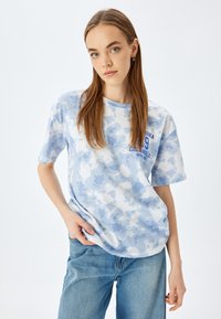 Camiseta de algodón suave en tono azul claro con efecto tie-dye, de mangas cortas, con un escote tipo crew y un estampado gráfico en un azul oscuro contrastante.