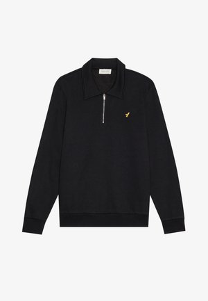 Fekete pulóver, zipzárral a nyaknál, texturált anyagból készült. Jellemzője egy lapos gallér és egy kis arany madár logó a mellrészen.