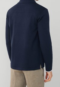 Camicia a maniche lunghe blu navy con colletto, tessuto texturizzato, dettagli sulla cucitura della spalla e fessure laterali nell'orlo.